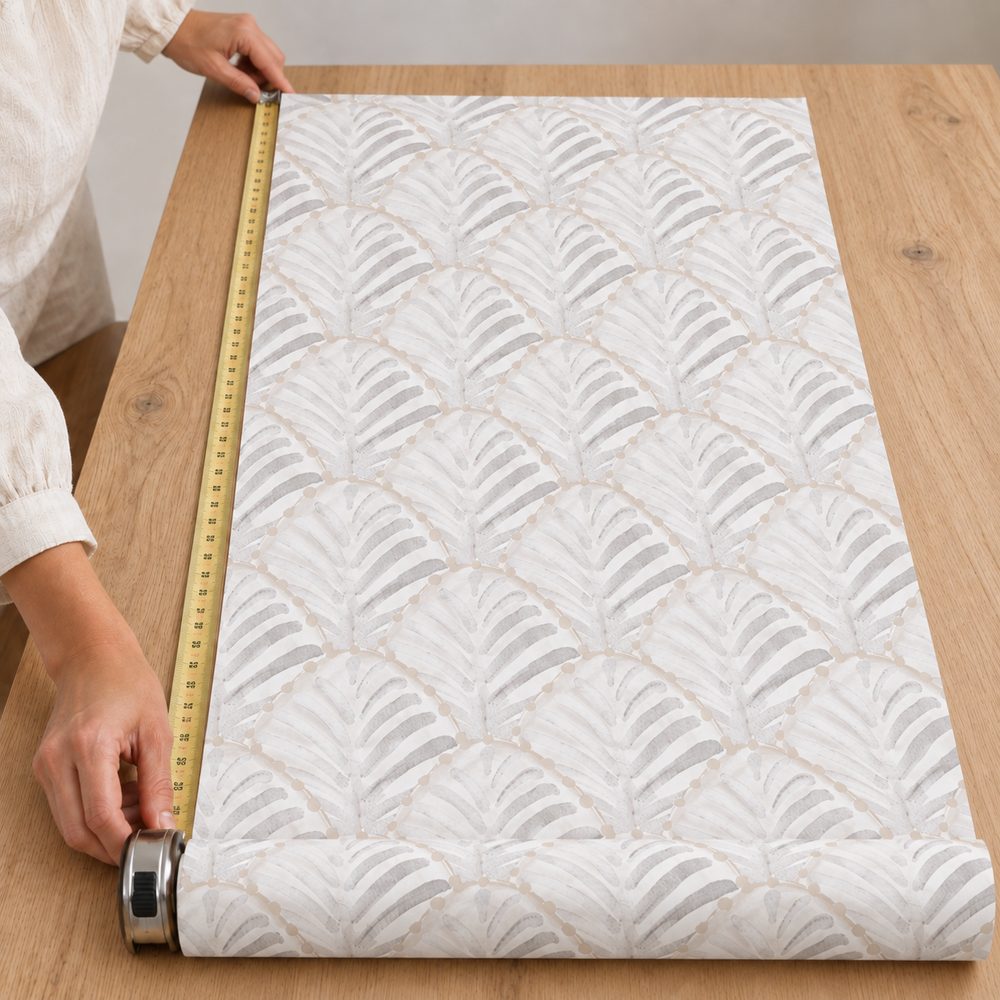 Manos midiendo una tira de papel pintado sobre una mesa.